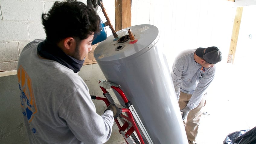 Angel Gomez (L) and Franes Mendez, technicians at heating, cooling and plumbing company John G. Webster, remove a gas water heater from a home in Washington, D.C., on August 28, 2024. 