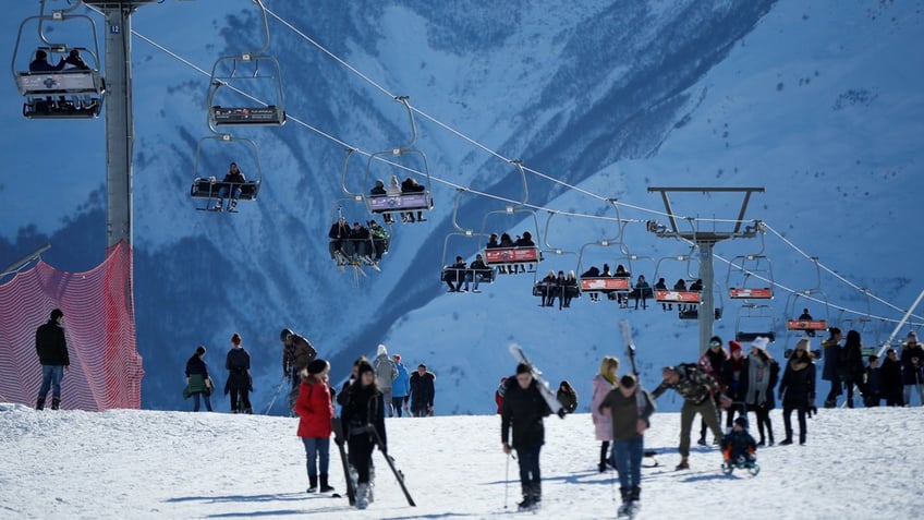 Skiers ride a ski lift and walk on the snow at Gudauri ski resort in Georgia.