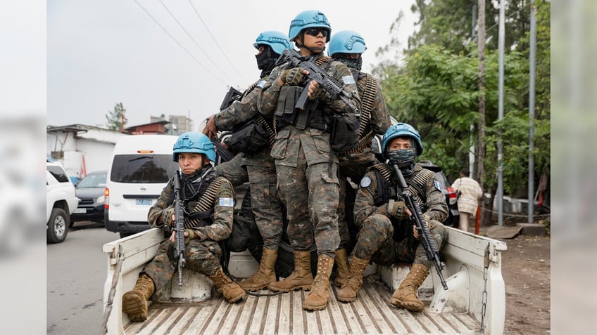 Members of the United Nations Organization Stabilization Mission in the Democratic Republic of the Congo ride on a pickup truck. They are armed, dressed in military fatigues, and wearing the blue helmets characteristic of U.N. forces.