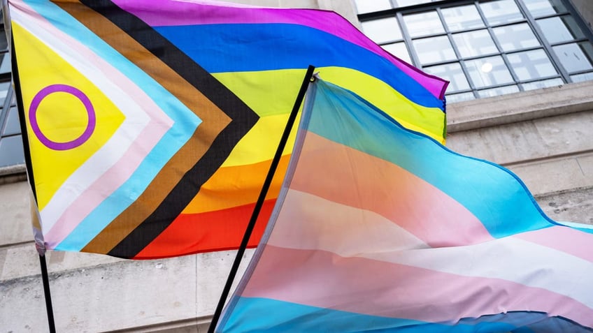 transgender flag flying aside an LGBTQIA+ flag