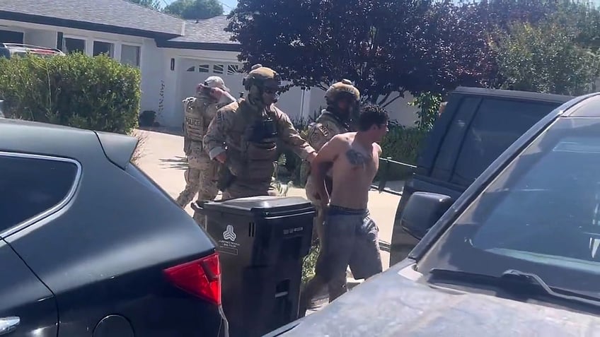 federal officials escort shirtless suspect from house to vehicle