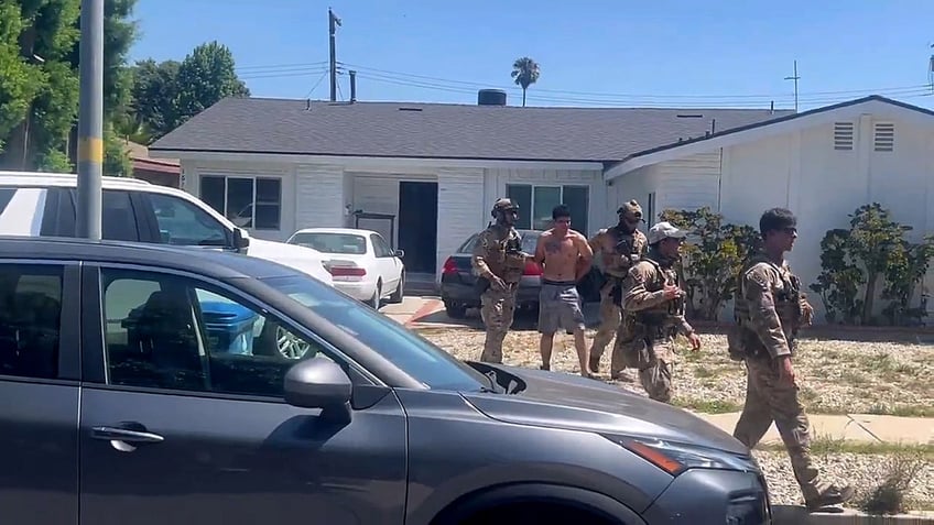federal officials escort shirtless suspect from house to vehicle