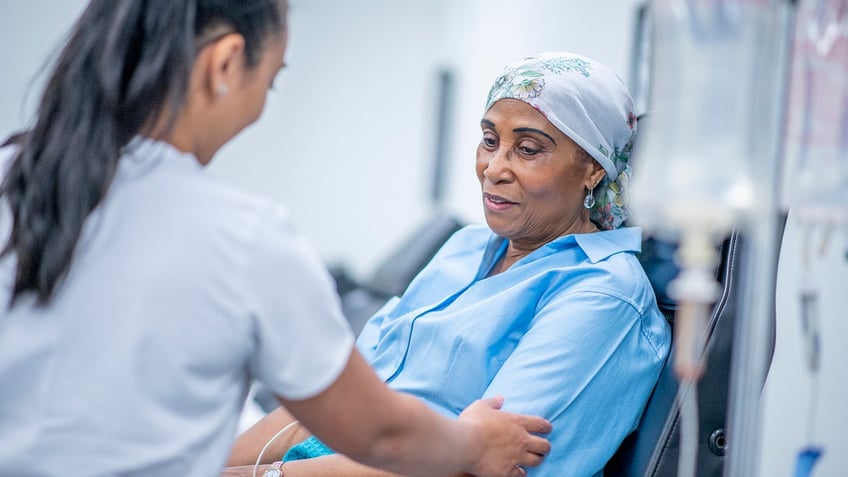 A woman wearing a head scarf recovers from chemo treatment in the hospital