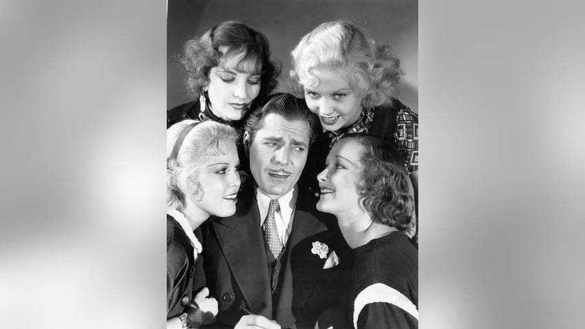 Warner Baxter surrounded by smiling actresses