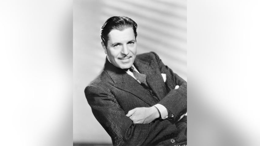 A close-up of Warner Baxter in a suit smiling for a glamour old Hollywood photo.