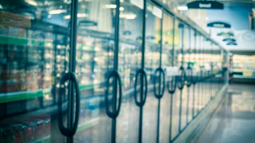 A blurry view of a grocery store freezer aisle is shown.