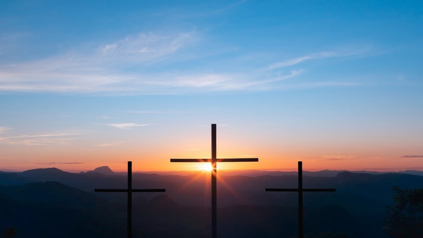 Three crosses on top of a mountain with the sunset in the background