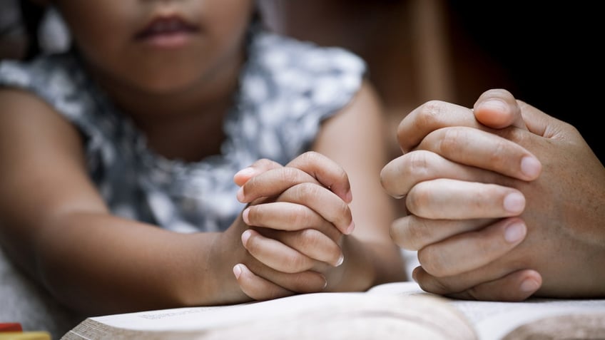 Mother and little girl hands folded praying. 