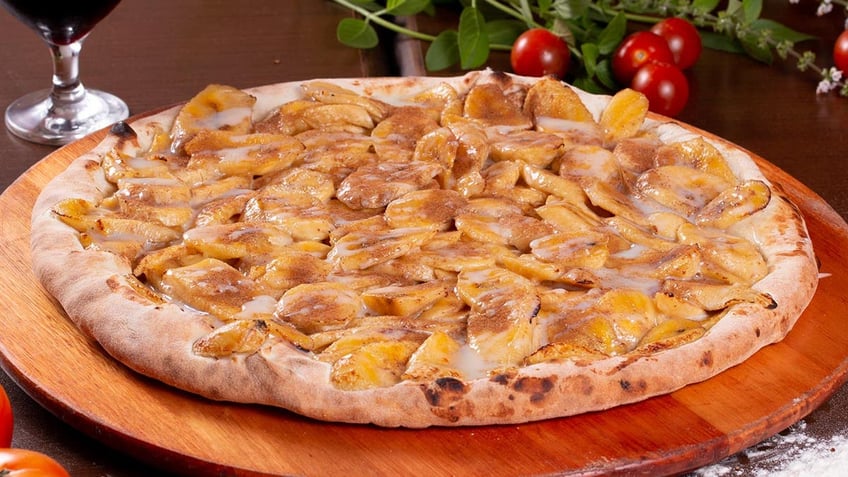 A banana pizza sits on a wooden board