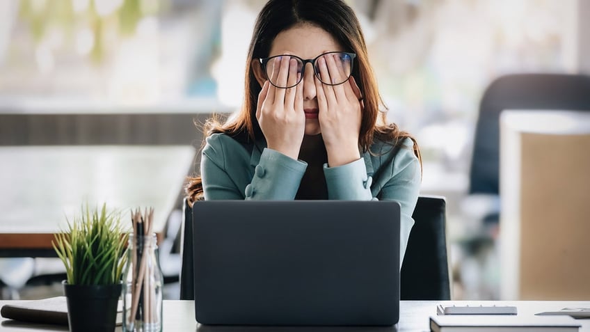 Woman rubbing her eyes at work