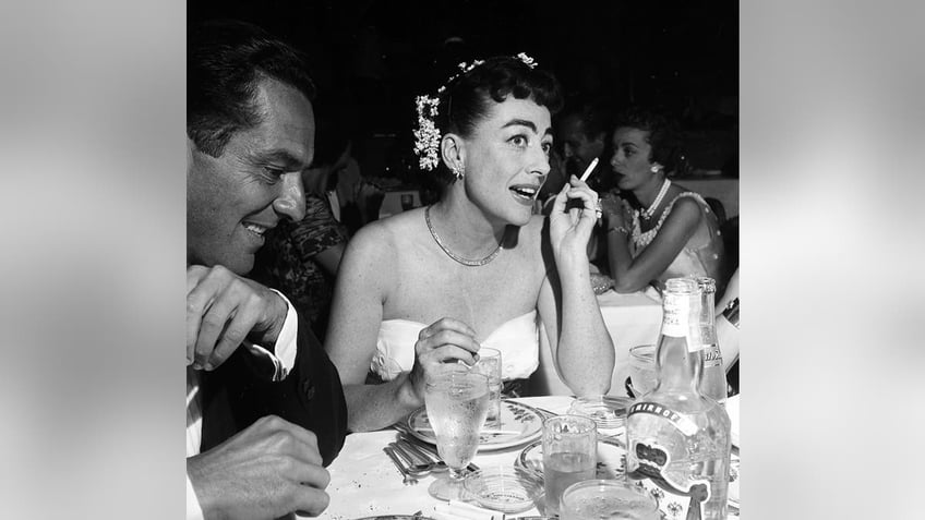 Scott Huver smiling next to Joan Crawford at a dining table.