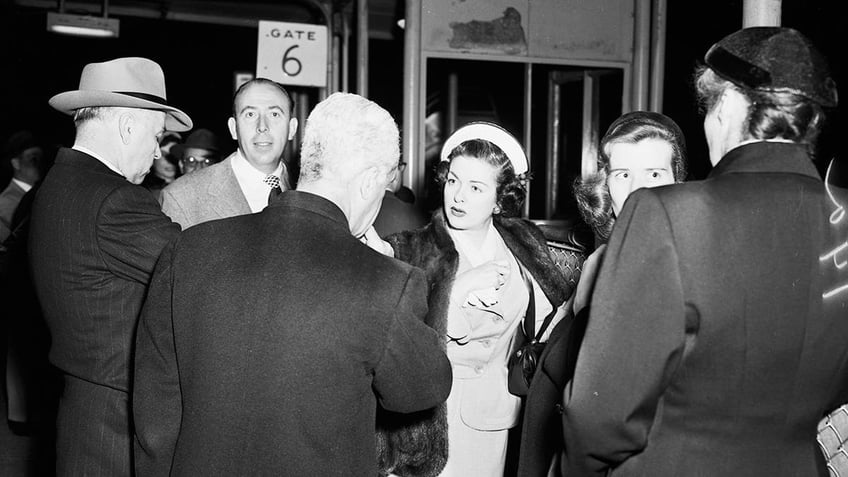 Joan Bennett being surrounded by photographers and reporters looking bewildered.