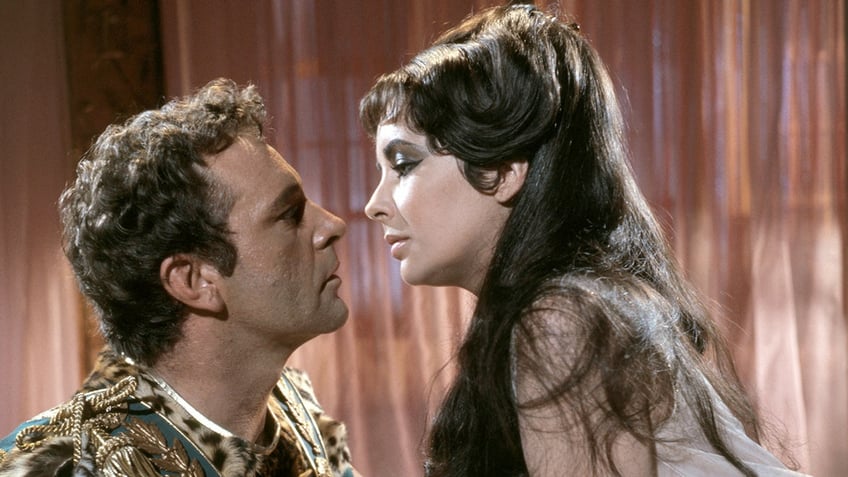 Richard Burton and Elizabeth Taylor in costume about to kiss each other.