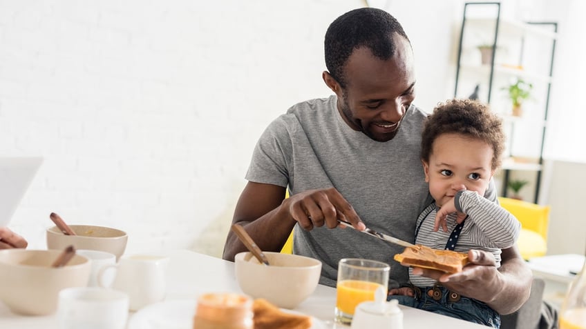 father applying peanut butter on toast for little son