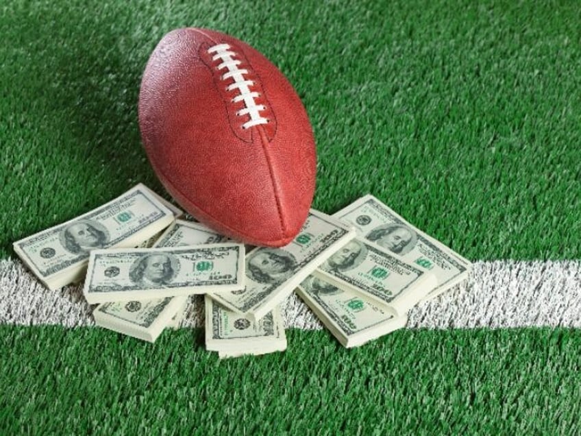 An NFL football sits with a pile of money on a green field