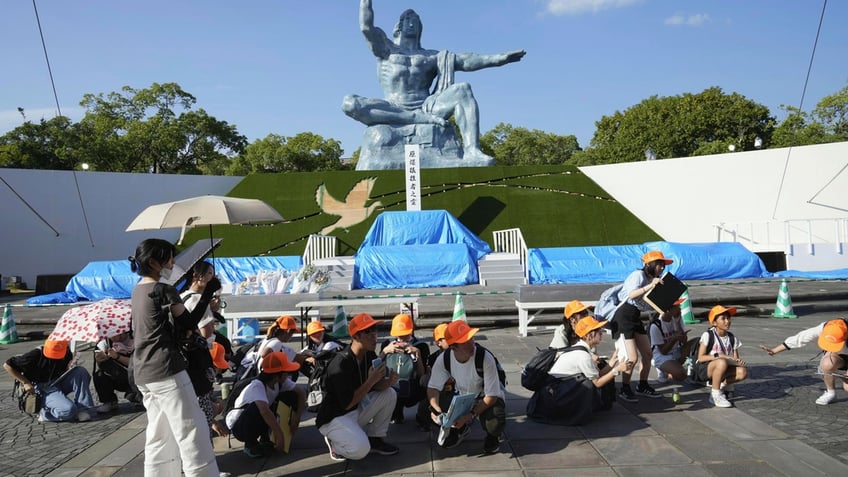 Visitors to Nagasaki's Peace Park wearing yellow hats crouch after an earthquake alert is issued.