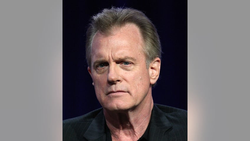 Stephen Collins in a black shirt looks serious on stage 