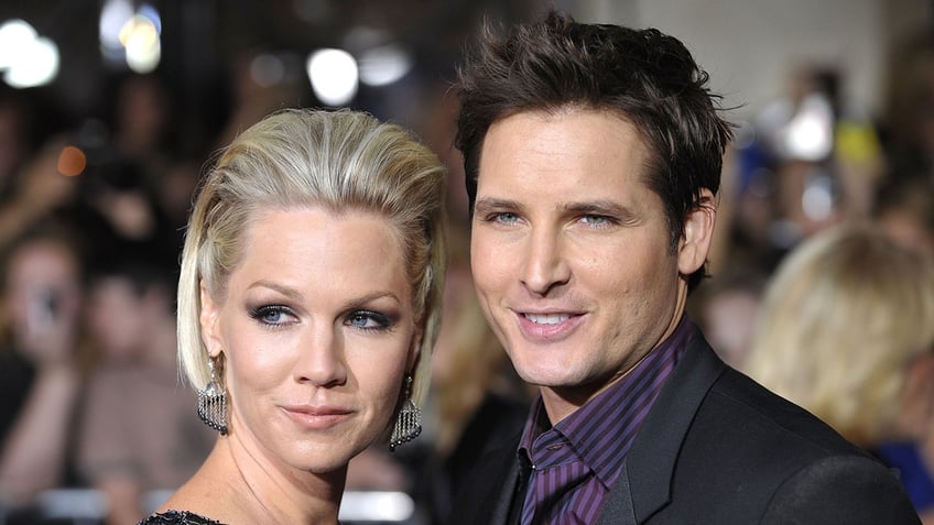 Jennie Garth looks to her right on the carpet as Peter Facinelli in a black suit and purple shirt smiles