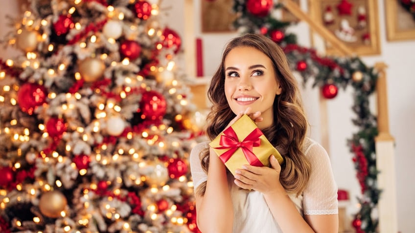 Woman holding up Christmas gift in front of decorated tree