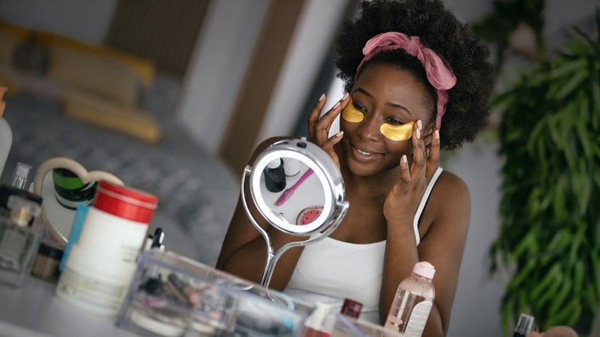 Woman doing self-care routine with gold under eye masks applied