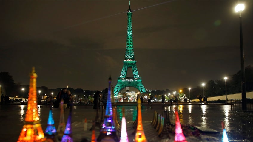 Small-gift Eiffel Towers are seen in front of the Eiffel Tower illuminated in green with the words "Paris Agreement is Done" on Nov. 4, 2016 in Paris, France. 