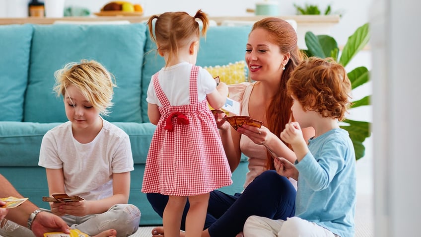 A happy family playing a card game together on the floor at home. A woman and three children. All have red hair.