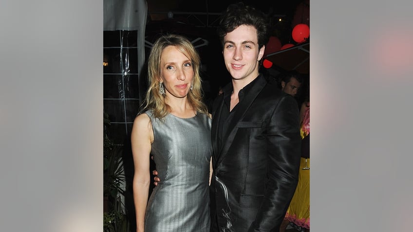Sam Taylor-Wood in a grey/silver dress stands next to Aaron Johnson in a black suit in Cannes