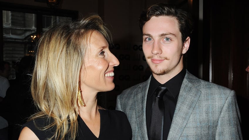 Sam Taylor-Wood looks lovingly at Aaron Johnson in a grey suit and black shirt and tie