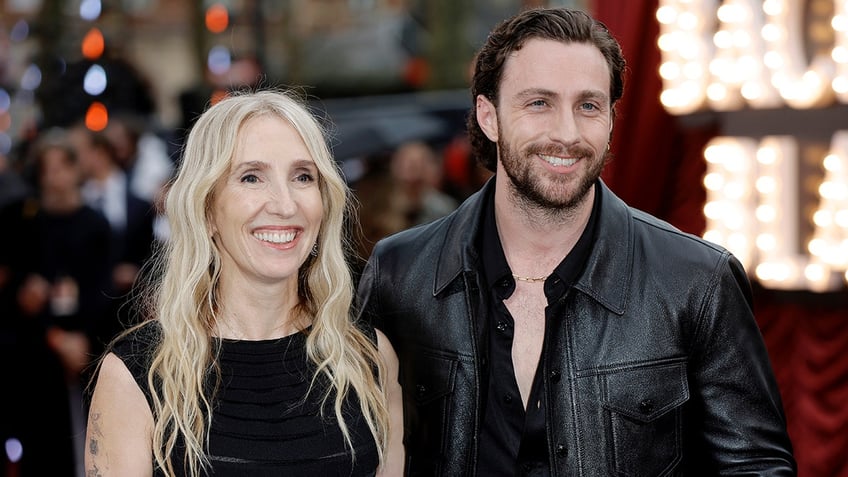 Sam Taylor-Johnson in black and husband Aaron Taylor-Johnson in a black suit smile on the carpet