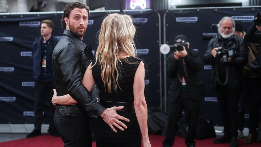 Aaron Taylor-Johnson looks over his shoulder as he holds his wife's lower back on the carpet