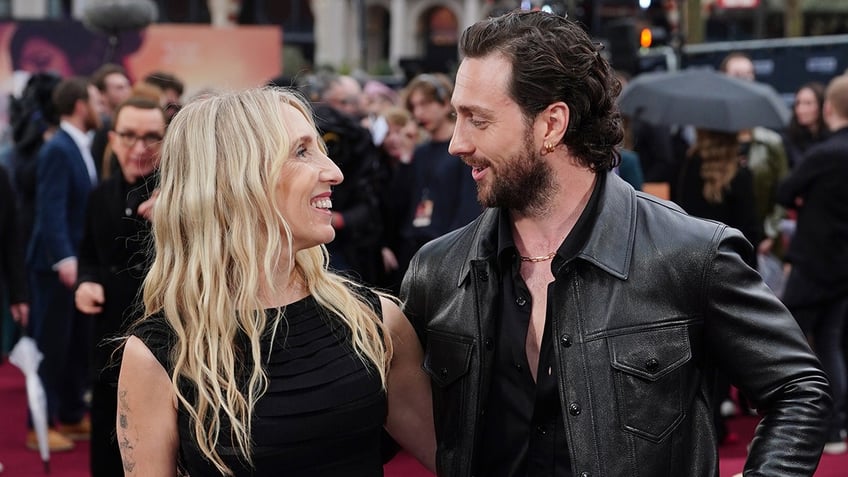 Sam Taylor-Johnson and husband Aaron Taylor-Johnson smile and look at each other on the carpet