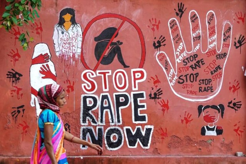 A woman walks past a mural painted on a wall in Ajmer condemning the rape and murder of a