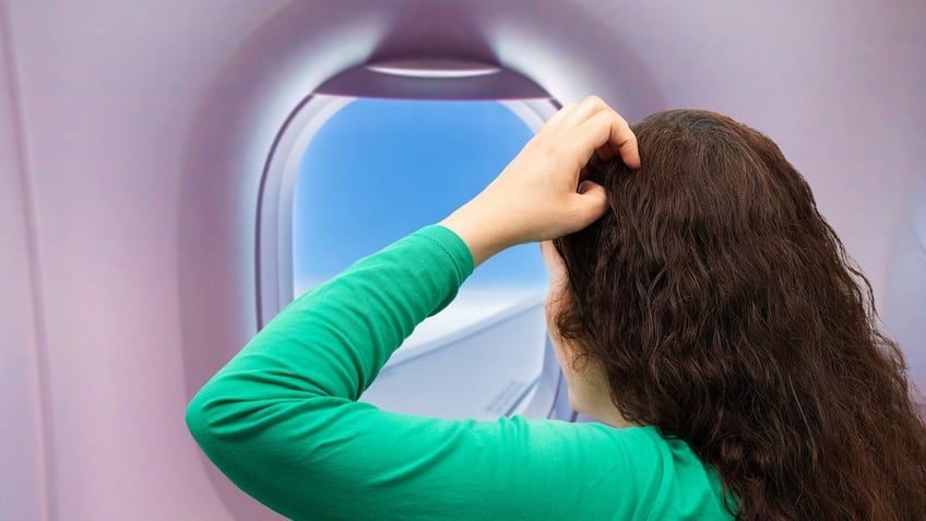 woman with her hand on her head and looking out the window inside the plane