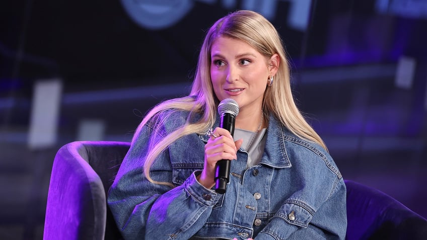 Meghan Trainor sitting in a chair holding a microphone