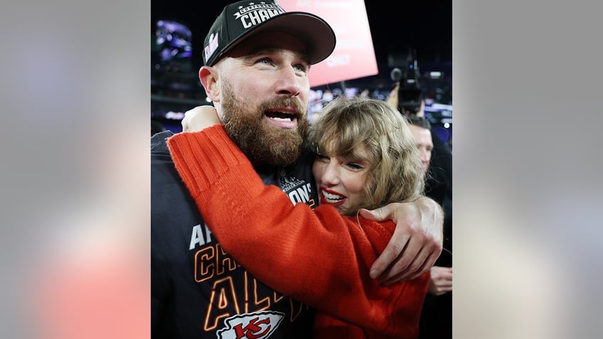 Taylor Swift in red holds on to Travis Kelce wearing an AFC Championship hat on the field