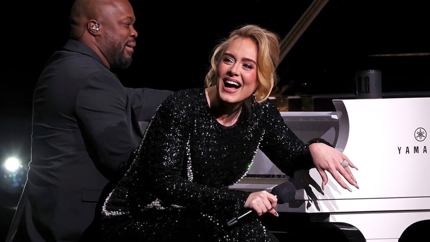 Adele laughs in a sparkly black dress while she sits next to her pianist during her Weekends with Adele show in Las Vegas