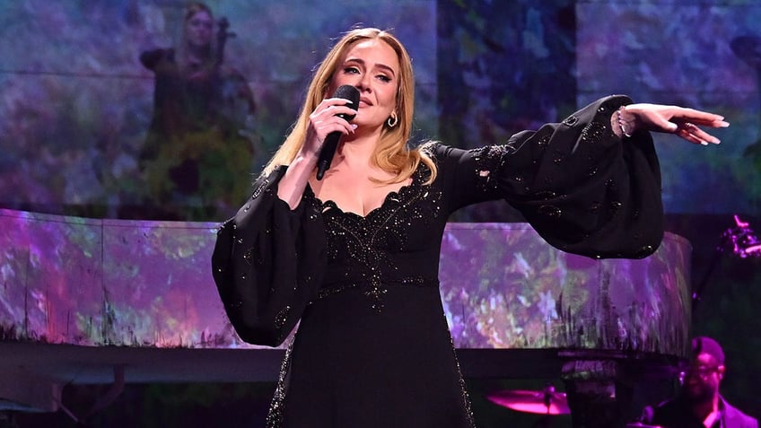 Adele singing on stage with her arm outstretched