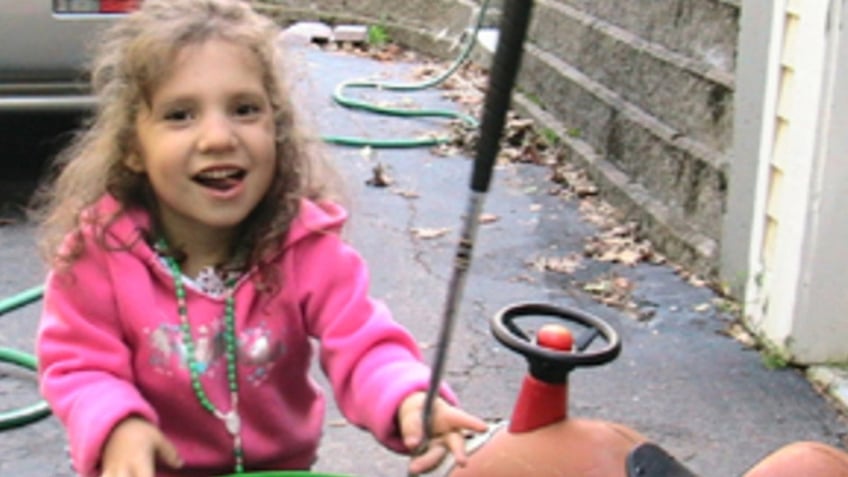 Natalia Grace wearing a pink sweater standing next to a toy car