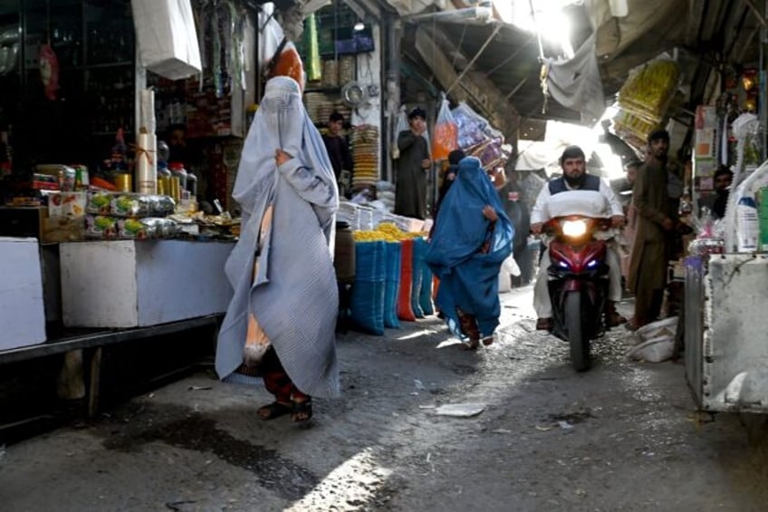 Afghan burqa-clad women walk through a market in Kandahar