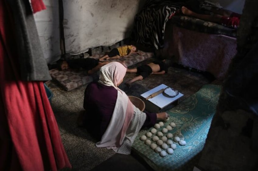 A displaced Palestinian woman prepares bread as children sleep in a tent at a school in th