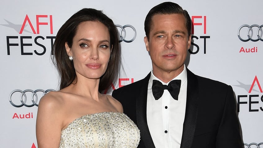 Angelina Jolie in a white and cream beaded strapless dress looks to her right with Brad Pitt, wearing a classic tuxedo also looking to his right