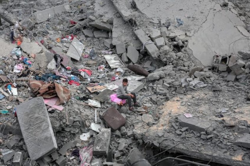 A boy sits among the rubble and scattered belongings of a home destroyed in an Israeli str