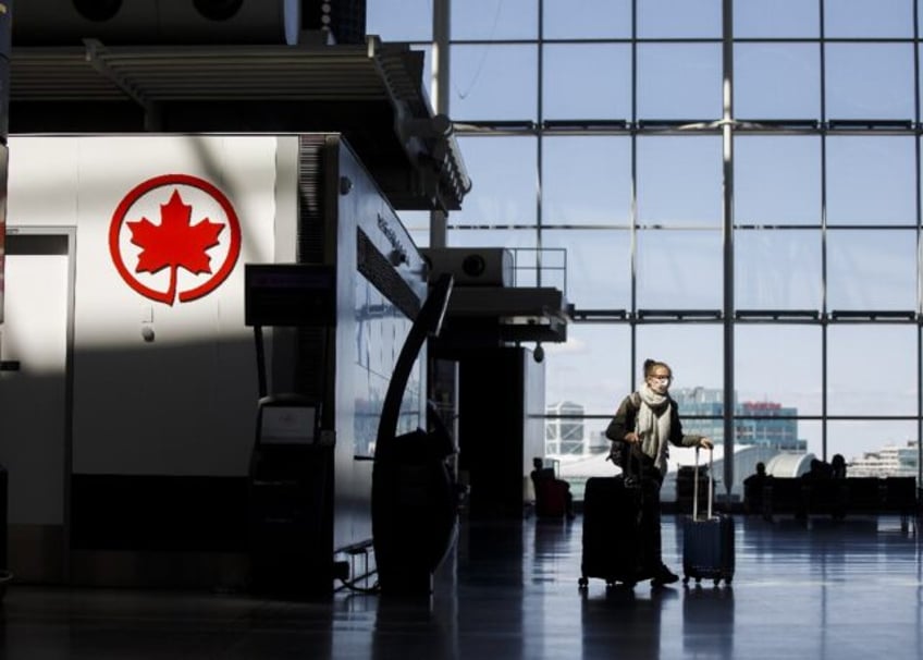 A passenger wheels her luggage near an Air Canada logo at Toronto Pearson International Ai