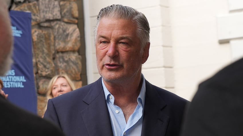 Alec Baldwin in a blue button down and navy suit is photographed at an event in New York