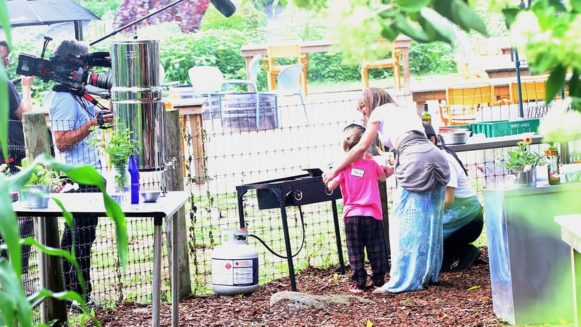 Hilaria Baldwin wraps a coat around her wait at a park.