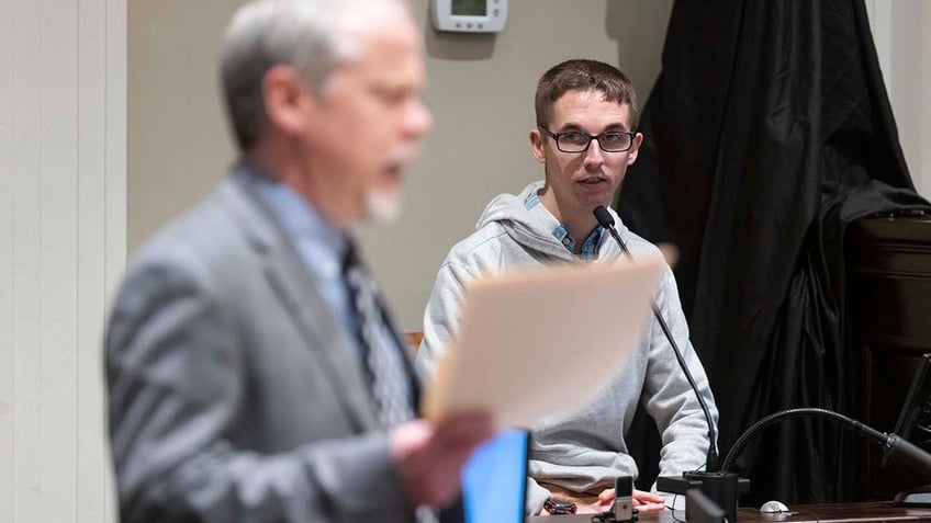 A man testifies while on the witness stand inside a courtroom.