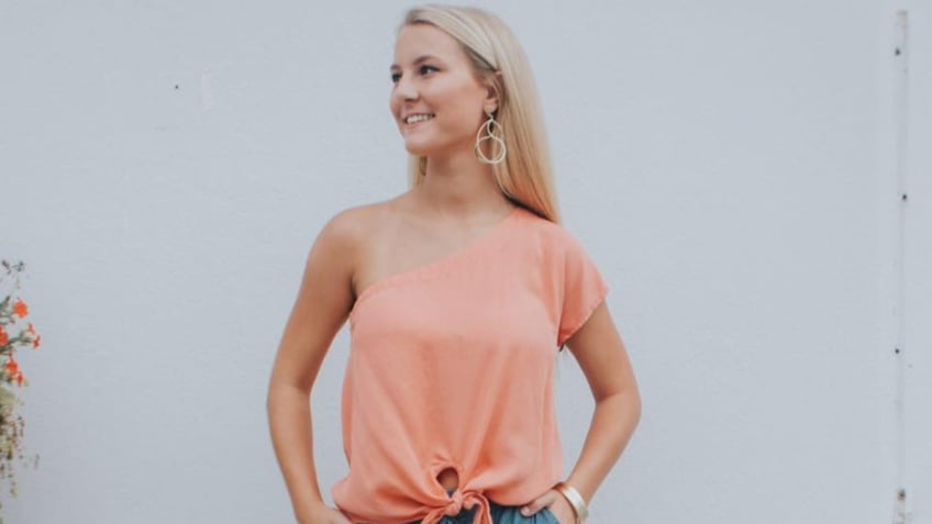 Mallory Beach smiles in a pink blouse with blonde hair and earrings