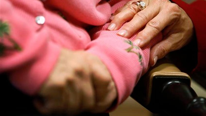A worker at an Alzheimer's assisted-living site puts her hand on the arm of a resident