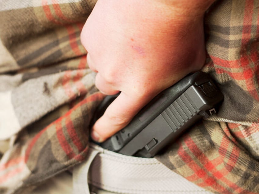 A man drawing a modern, polymer, .45 caliber semiautomatic pistol from inside the waistban