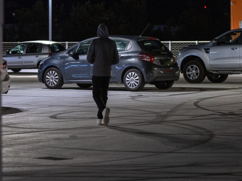 Man walking in outdoors car parking space at night.